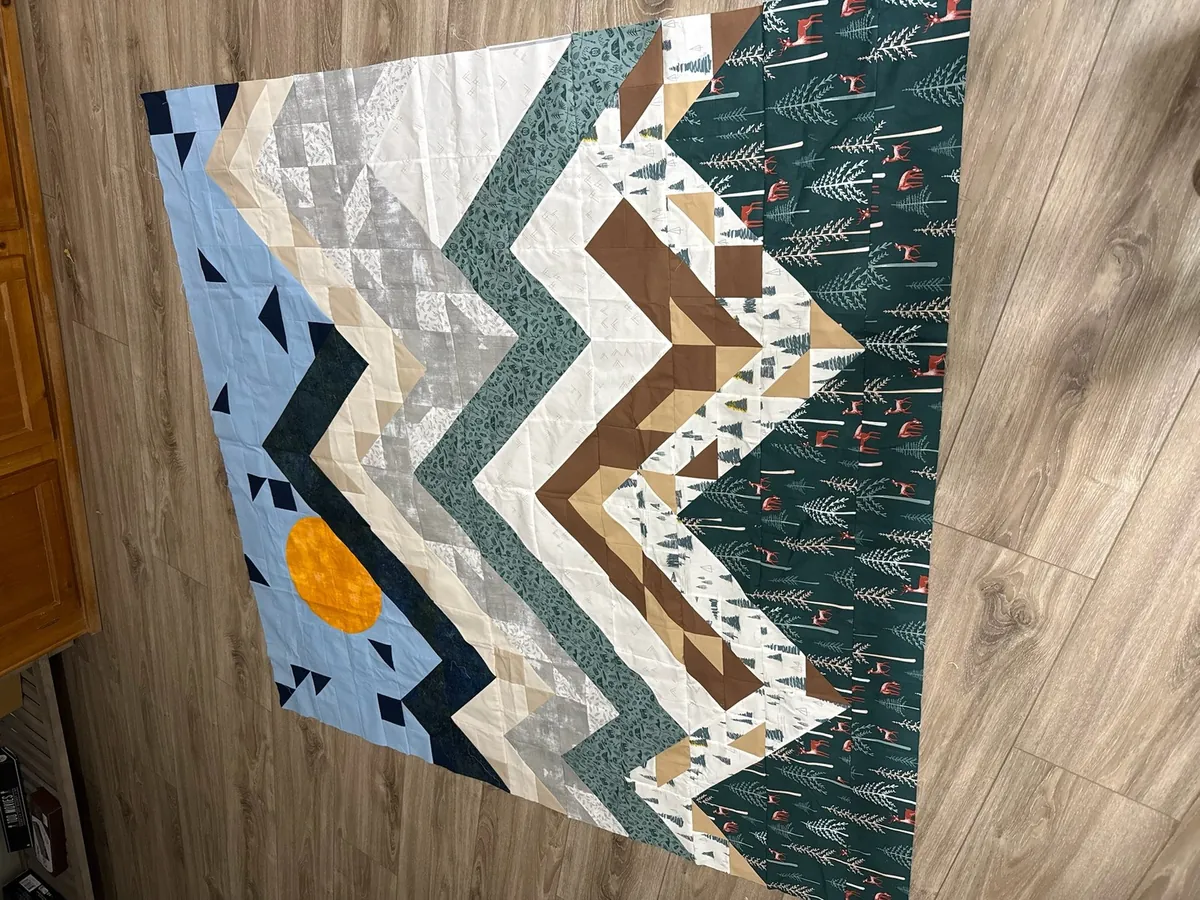 A custom mountain and forest quilt with an orange sun